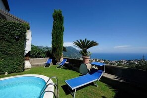 Un espace piscine avec des chaises longues bleues et une vue sur la mer et les montagnes.