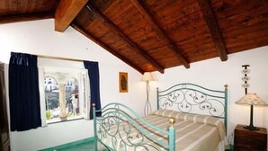 A bedroom with a metal bed frame, a window with curtains, a bedside lamp, and a wooden ceiling. - Apartment with Private Pool (SCALA)