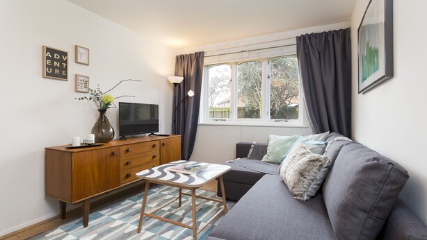 Ein modernes Wohnzimmer mit einem grauen Sofa, einem Holzschrank, einem Fernseher und einem gemusterten Teppich.