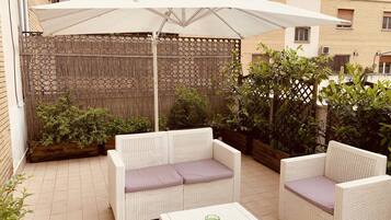 Een terrasgedeelte met rieten meubels, een witte parasol en potplanten.