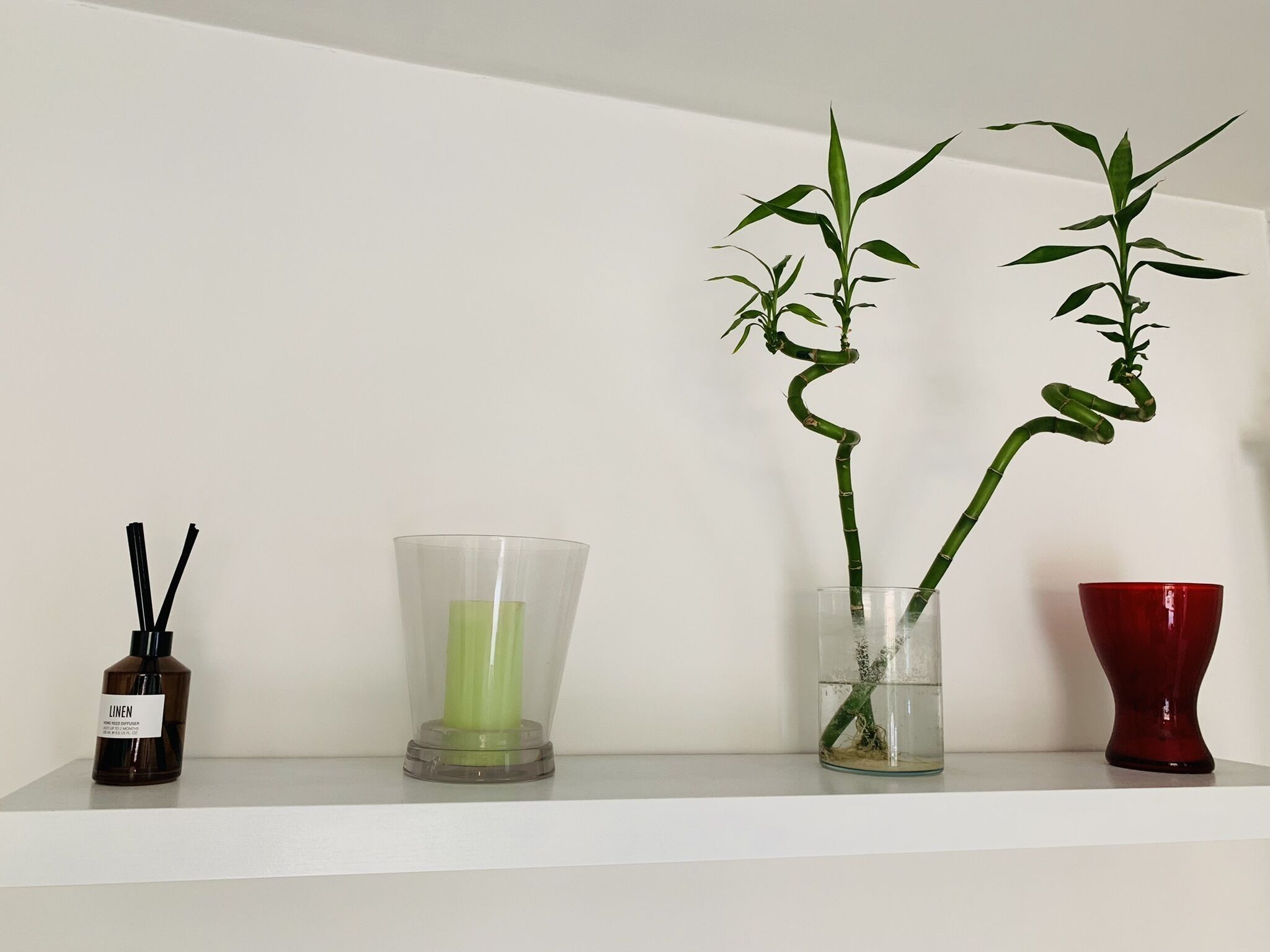 Een plank met drie vazen: een bruine fles, een heldere vaas met een groene kaars en een heldere vaas met een bamboeplant.
