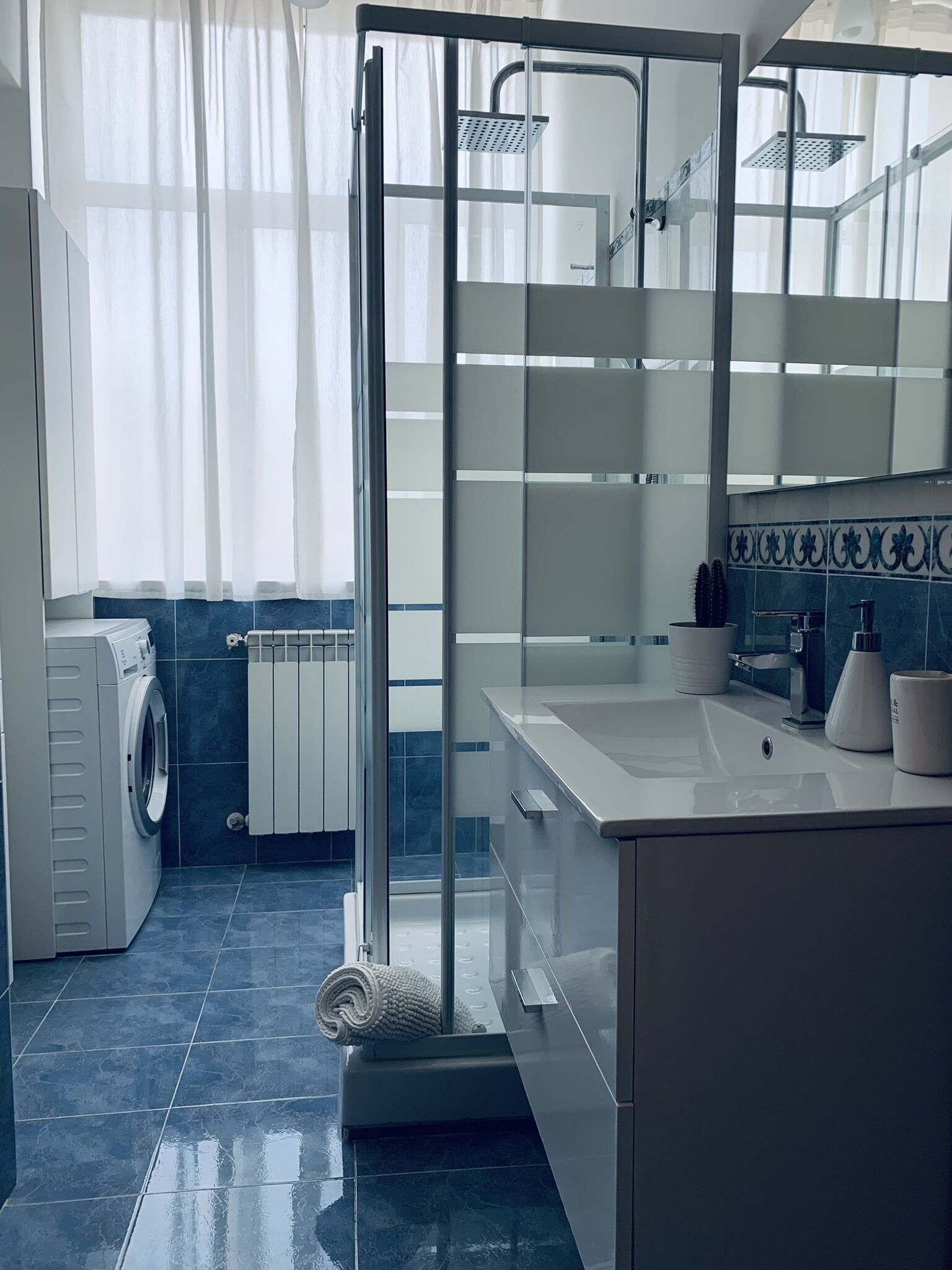 Une salle de bain moderne dotée d’une douche à parois de verre, d’un lave-linge encastré et d’un grand miroir.