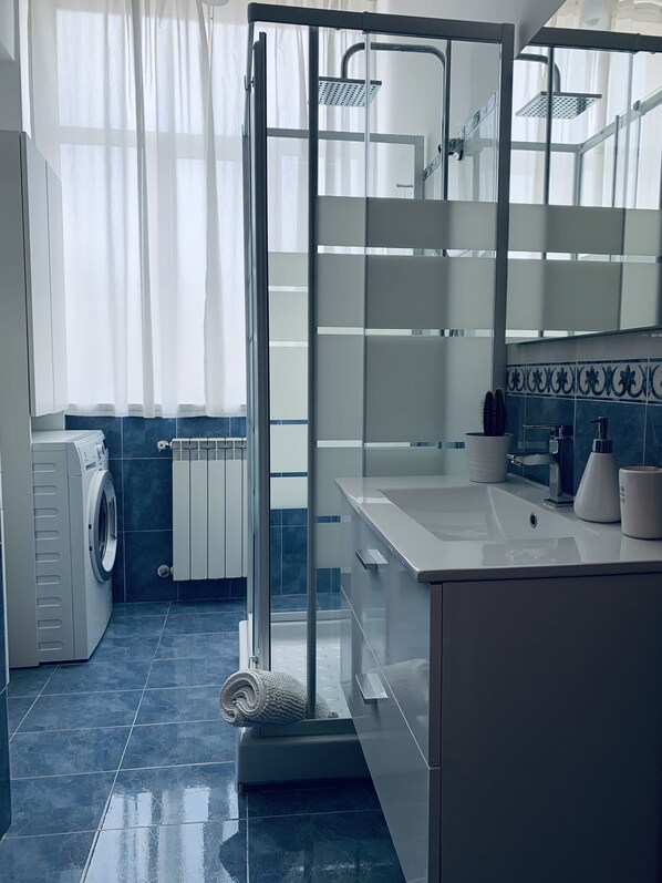 A modern bathroom with a glass shower enclosure, a built-in washing machine, and a large mirror.