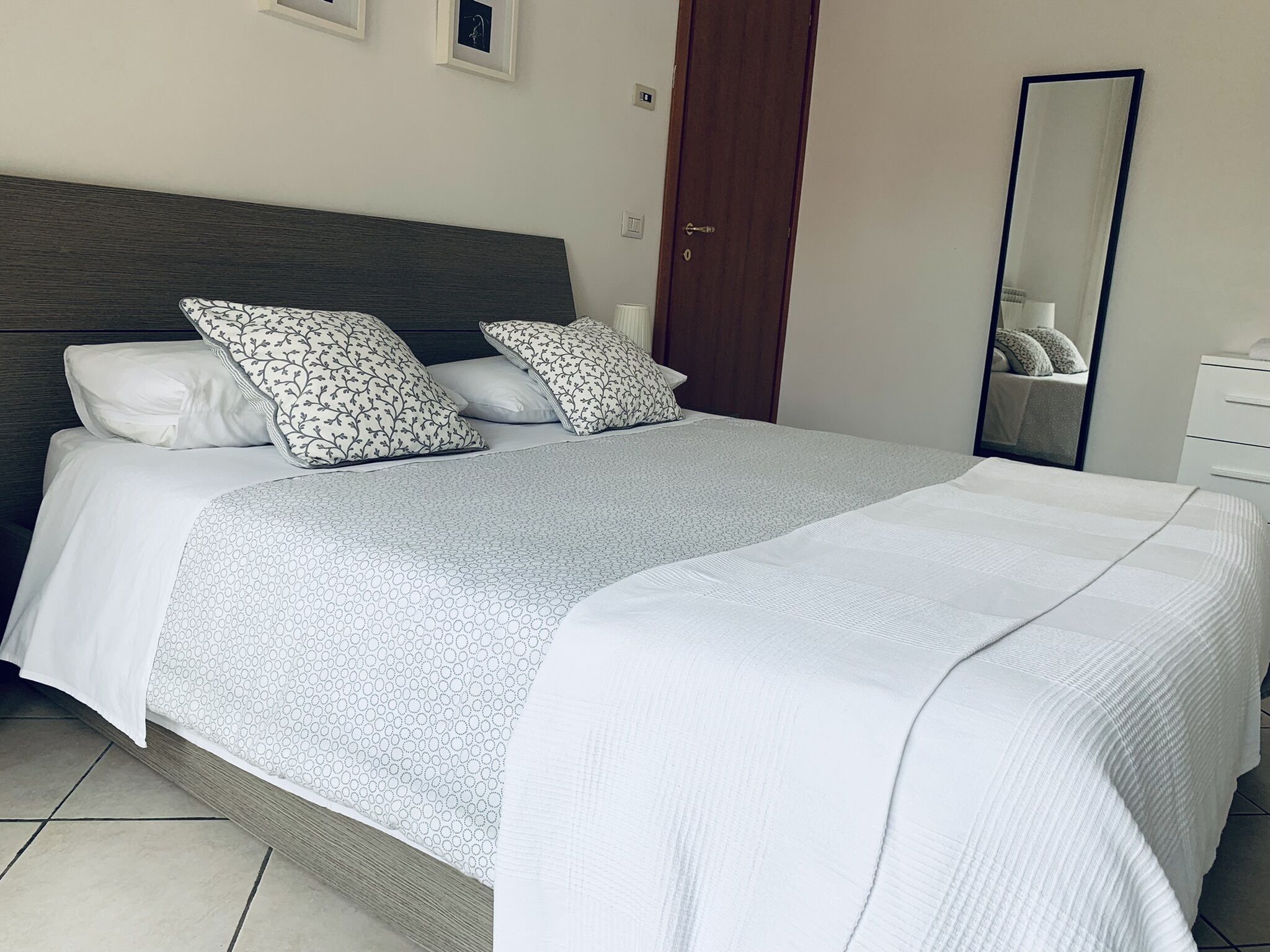 Un lit bien fait, recouvert d’une couvre-lit à motifs gris et blancs, avec deux oreillers assortis et une tête de lit en bois.