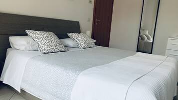Un lit bien fait, recouvert d’une couvre-lit à motifs gris et blancs, avec deux oreillers assortis et une tête de lit en bois.