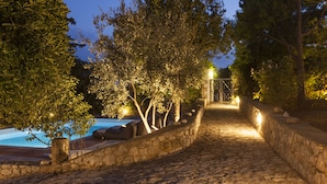 A stone pathway leading to a pool area, surrounded by trees and stone walls. - Luxurious Mani Peninsula Traditional Tower (East Mani)