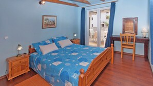 Une chambre à coucher avec un lit en bois, un bureau avec une chaise, une table de chevet et une fenêtre avec des rideaux.