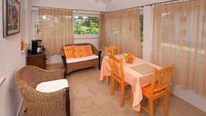Un coin repas avec une table dressée pour deux personnes, des chaises en osier et un canapé en osier agrémenté d’un coussin.