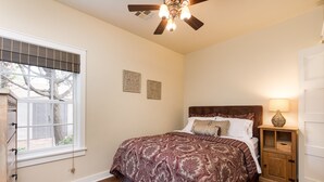 Ein Schlafzimmer mit einem großen Bett, einem Deckenventilator, einem Fenster mit Jalousien und einem Nachttisch mit Lampe.