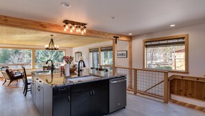 A spacious kitchen with a large island, wooden beams, and large windows offering views of the outdoors. - Peshastin River Place-Riverfront near Leavenworth (Peshastin)