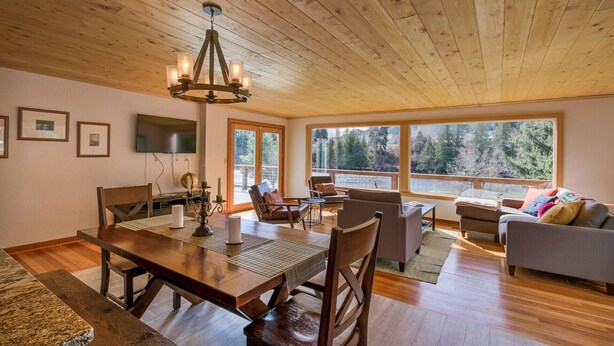 A spacious living area with a wooden ceiling, a dining table with chairs, a sofa, and a television mounted on the wall. - Peshastin River Place-Riverfront near Leavenworth (Peshastin)