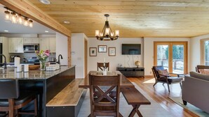 A spacious kitchen with a wooden ceiling, a dining area with a bench and chairs, and a living room with a sofa and a TV. - Peshastin River Place-Riverfront near Leavenworth (Peshastin)