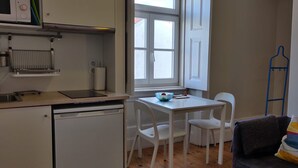 Une cuisine compacte équipée d’un lave-vaisselle, d’une petite table avec des chaises, d’une fenêtre avec des volets blancs et d’un porte-manteau bleu fixé au mur.