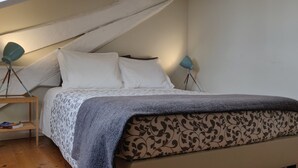 Une chambre à coucher avec un lit, deux lampes de chevet, une étagère remplie de livres et une couvre-lit à motifs.