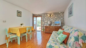 Una habitación con una mesa de comedor de madera, sillas, un sofá, un televisor y una pared de piedra.
