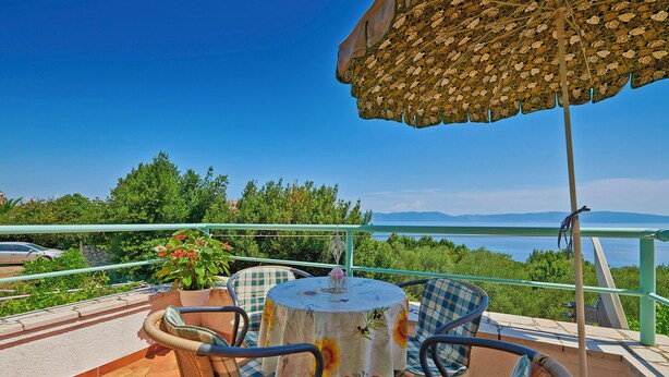 Una terraza con una mesa, sillas, una planta en maceta y vistas al mar y las montañas.