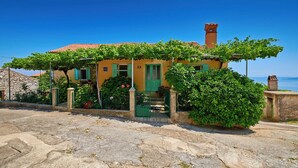 Una casa amarilla con techo de tejas rojas, contraventanas verdes y una chimenea.