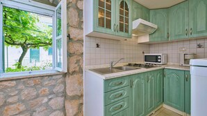 Una cocina con paredes de piedra, armarios verdes, una ventana con vistas a la vegetación y electrodomésticos básicos.