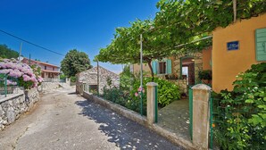 Una calle estrecha flanqueada por casas de piedra, un edificio de piedra y abundante vegetación.