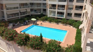 Un hotel de varios pisos con piscina rodeada de follaje y flores rojas.