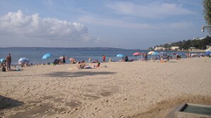 Una playa con gente tomando el sol y nadando, sombrillas y un cielo despejado.