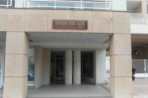 The entrance to Riviera Port Azur, featuring a sign with the name and address, a covered entrance with columns, and a view of the surrounding area.
