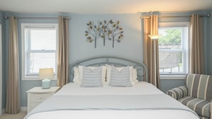 A bedroom with a bed, a nightstand, a lamp, a chair, and a wall art piece.