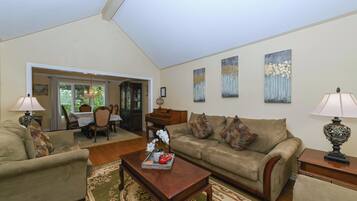 A spacious living room with a high ceiling, a dining area with a table and chairs, and a sofa set.