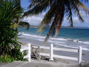 A beach with a white fence, palm trees, and the ocean. - La Terrasse du Rocher (Le Diamant)