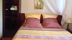 Ein Bett mit gemusterten Textilien, ein Holzschrank und ein an der Wand befestigtes Kunstwerk.