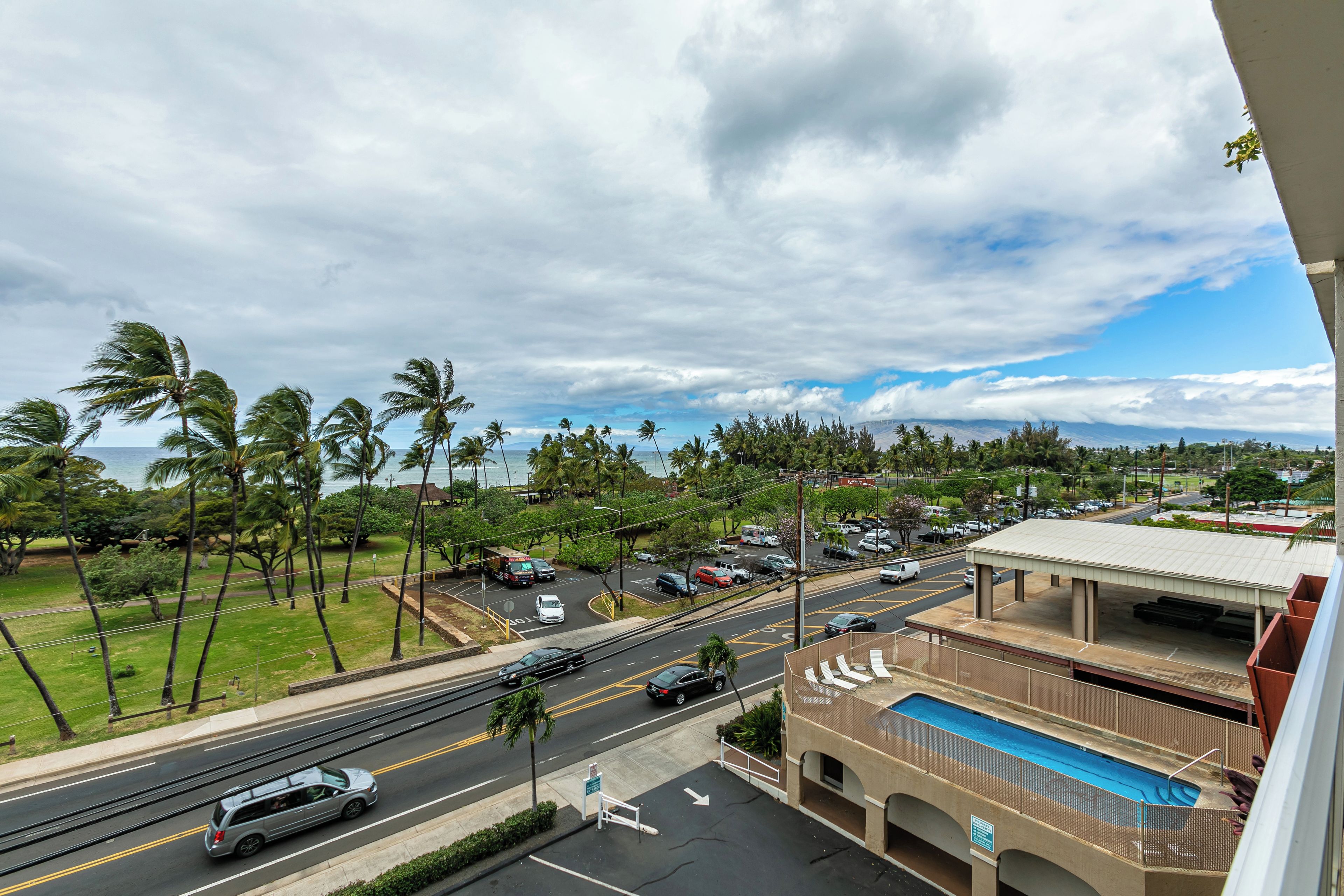 A view of a street with cars, palm trees, and a building with a pool.