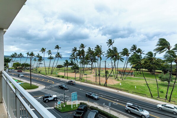 A view from a balcony overlooking a busy street with palm trees and a view of the ocean.
