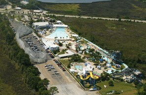Explore a vibrant theme park with thrilling water slides and roller coasters, surrounded by lush greenery.