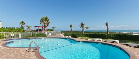 A large, curved swimming pool with a clear blue water, surrounded by a brick deck.