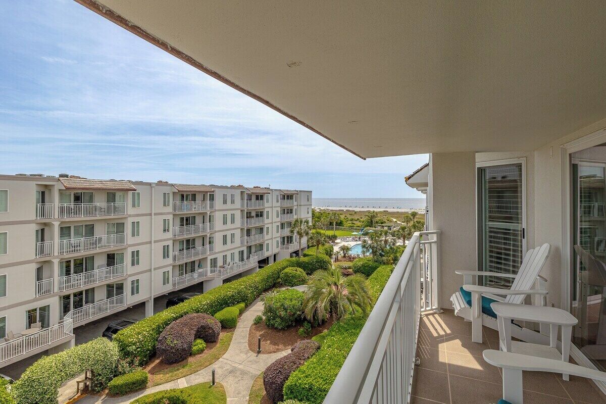 A balcony with white chairs and a view of a multi-story building with balconies.