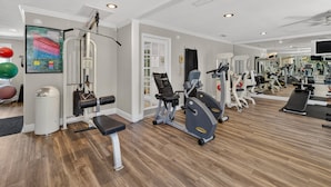 A gym with various exercise equipment, a mirror, and a wall-mounted screen.