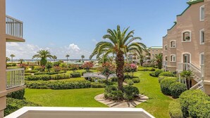 A hotel courtyard with manicured lawns, palm trees, and a view of the ocean.