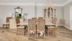 A dining area with a wooden table and wicker chairs, a chandelier, and a cabinet with glass doors.
