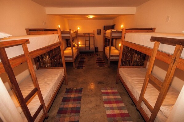 Une chambre de dortoir avec des lits superposés alignés, un tapis à motifs sur le sol et un luminaire au plafond.