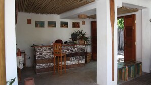 A reception area with a wooden desk, a chair, and a bench. There are framed pictures on the wall and a plant on the desk. - Hostel e Pousada Casa de Paixão (Porto Seguro)