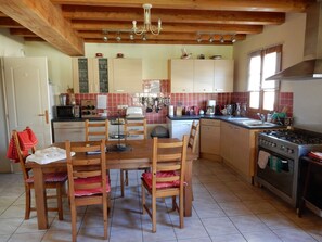 Une cuisine avec des meubles de rangement en bois, une table à manger avec des chaises, une cuisinière et un lustre.