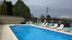 Una piscina rectangular con agua azul cristalina, rodeada por un muro de piedra y una solana con baldosas.