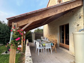Une terrasse couverte avec une table et des chaises, une pergola en bois et un mur en pierre.