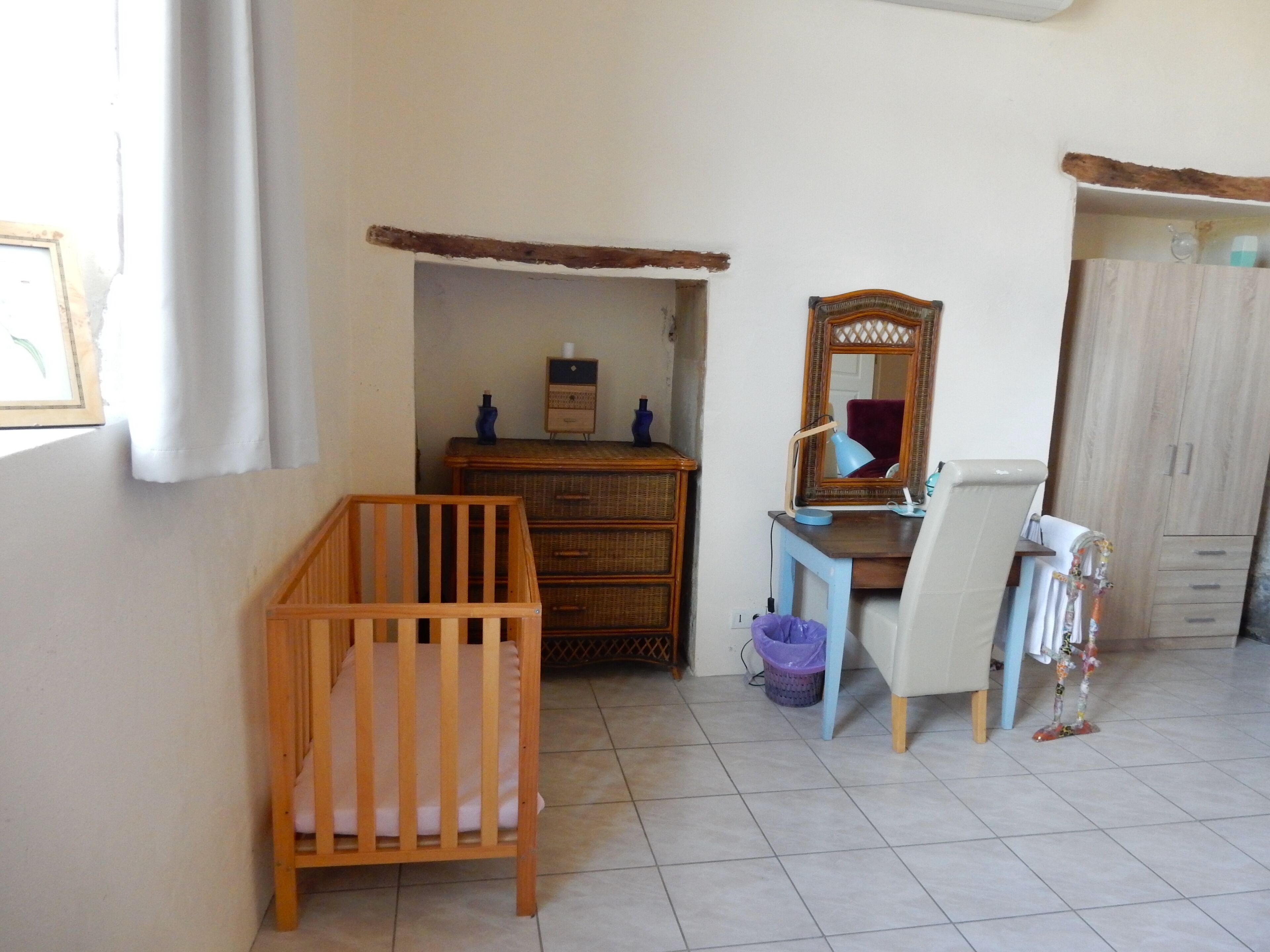 A room with a wooden crib, a dresser, a mirror, a desk with a lamp, and a radiator.