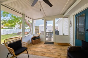 A covered porch with wicker chairs, a welcome mat, and a view of a backyard with a fence and trees.