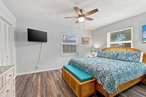 A bedroom with a bed, a ceiling fan, a TV, and a window with blinds. - Blocks from the Ocean in a Convenient and Desirabl (Saint Simons Island)