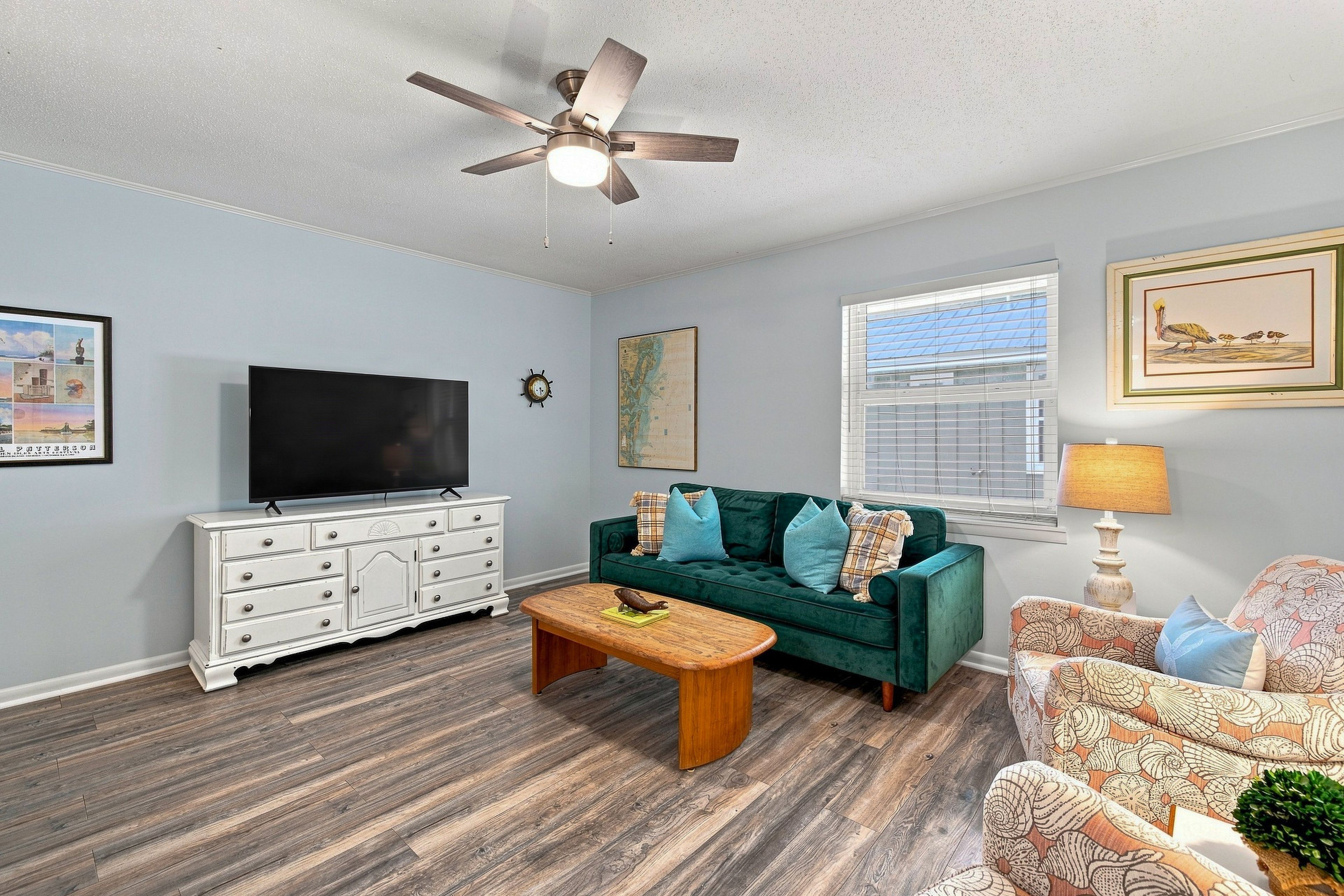A living room with a television, a green sofa, a wooden coffee table, and a ceiling fan.