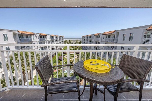 Varanda com cadeiras de vime e uma mesa redonda, com vista para uma piscina e edifícios com telhados vermelhos.
