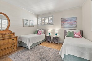 A bedroom with two single beds, a dresser, a mirror, a window with shutters, and a painting on the wall.