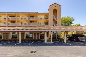 A multi-story hotel with a covered parking area and a black SUV parked in the lot.
